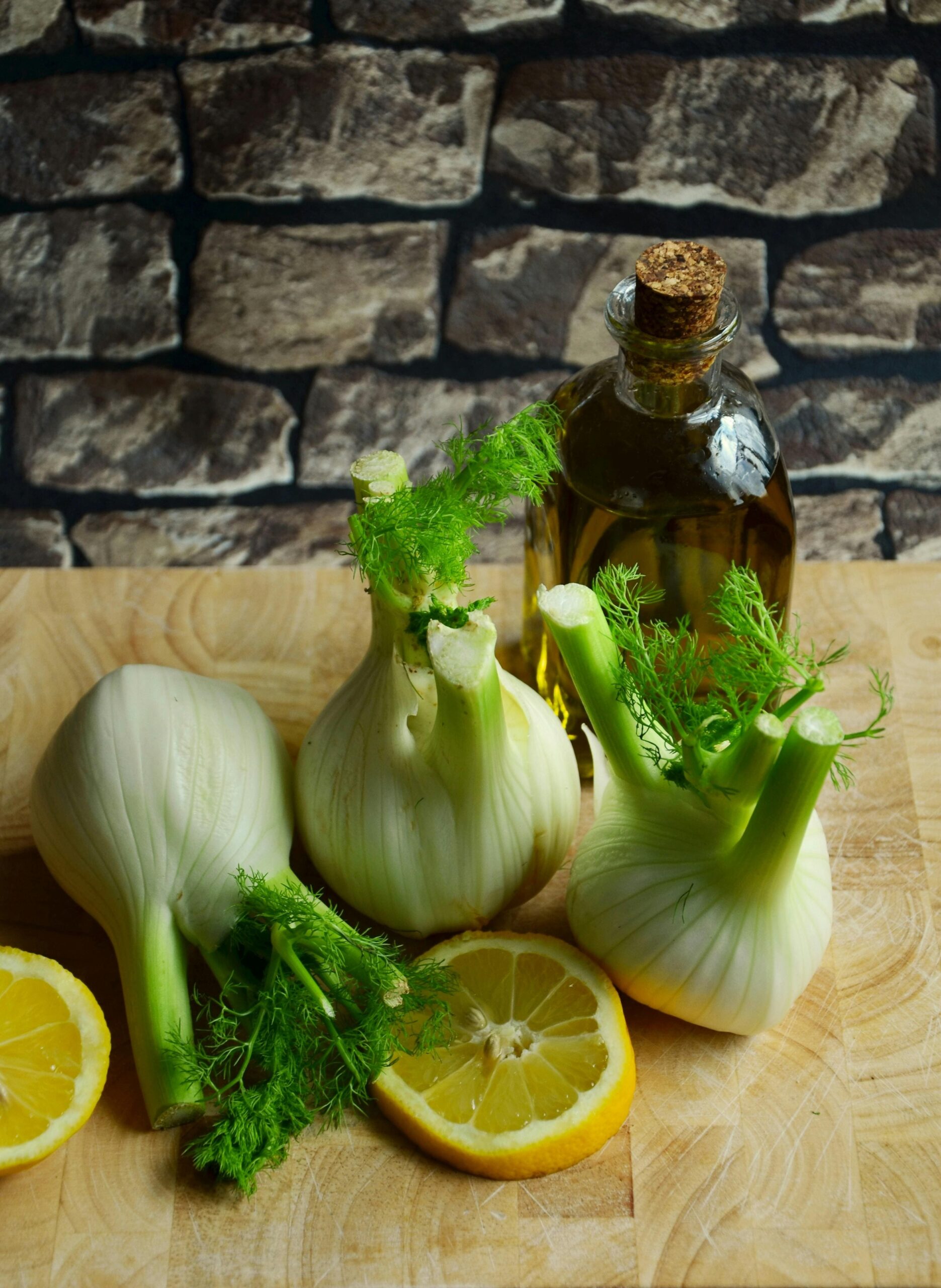 tagliere con 3 finocchi interi, due fette di limone e una bottiglia di olio